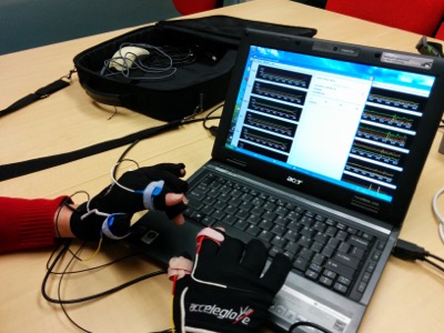 The new and old accelerometers gloves being tested on a participant's fingers while at a laptop.